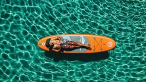 Relaxed man sunbathing on colorful paddleboard in clear blue water.